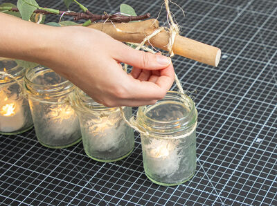 Hand wickelt Lichterkette um den Treibholzast. 