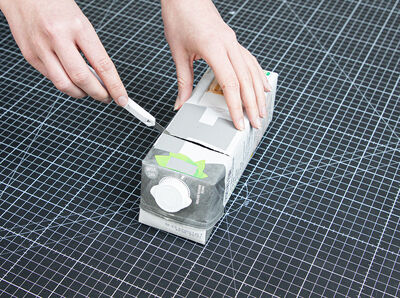 Hand h&auml;lt Cutter und schneidet Milchkarton.