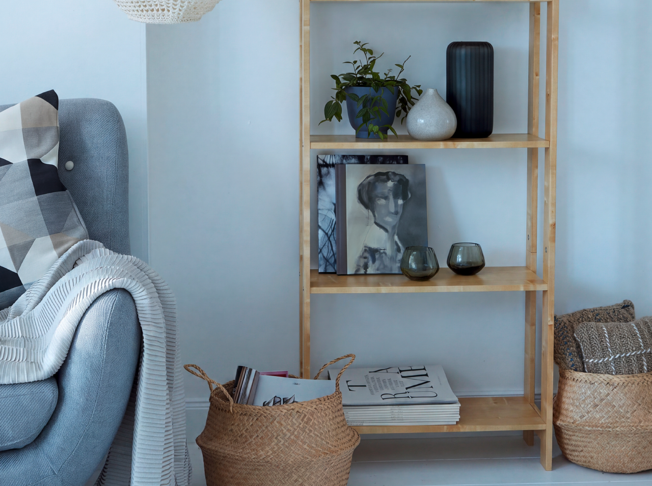 Gem&uuml;tliche Wohnecke mit hellem Sessel, dekorativem Holzregal und Pflanzen in modernen Wohnaccessoires.