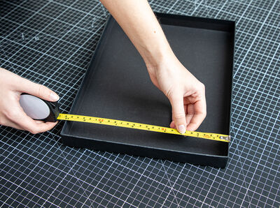 Hand spannt Ma&szlig;band innen im Kartondeckel zum Messen der L&auml;nge.