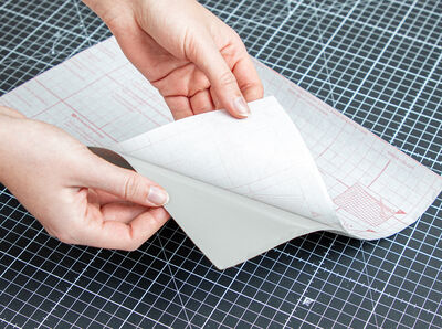 H&auml;nde halten Klebefolie, an deren R&uuml;ckseite das Schutzpapier eine Handbreit abgezogen ist. 