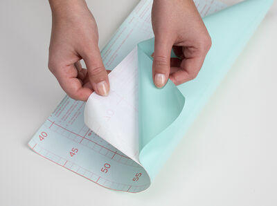 Hand zieht das R&uuml;ckseitenpapier der Folie ab.