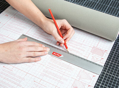 Hand h&auml;lt Stift, der Linie auf Rasterpapier zeichnet.