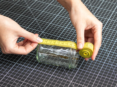 Hand mit Maßband misst Höhe des Glases unterhalb des Rands.