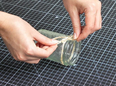 Hände binden Schnur um das Glas herum fest.