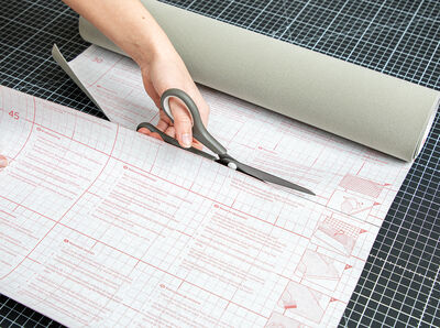 Hand h&auml;lt Schere und schneidet Folie entlang aufgezeichneter Linie.