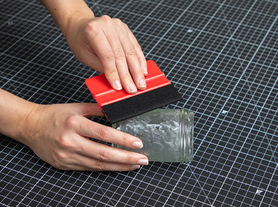 Rakel streicht über Glasfolie auf Schraubglas. 