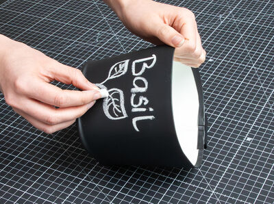 Hand h&auml;lt Kreidestift und beschriftet Tafelfolie auf &Uuml;bertopf.